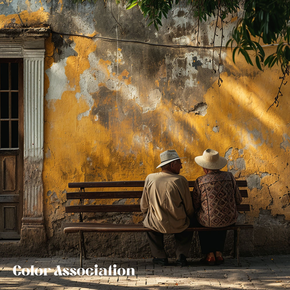 Elderly couple sitting on a bench against a weathered wall with peeling yellow paint.