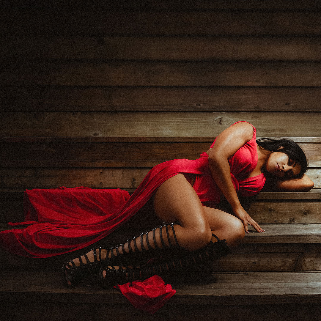 Fit latina model lying on the wooden steps in red dress and gladiator boots
